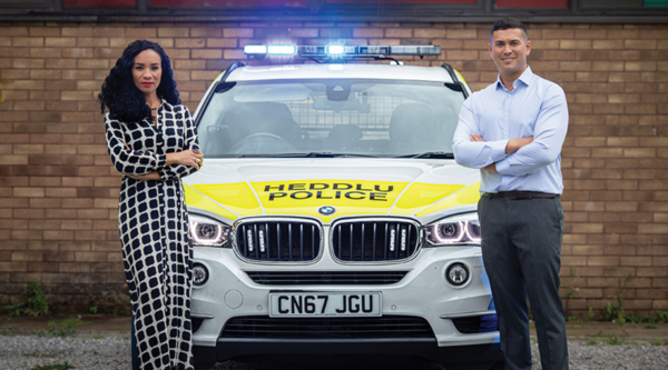 Michelle Ackerley and Rav Wilding fold their arms in front of a police car with its emergency lights on