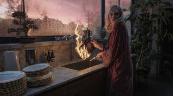 Cate Blanchett holds a burning book in a kitchen sink, looking over her shoulder