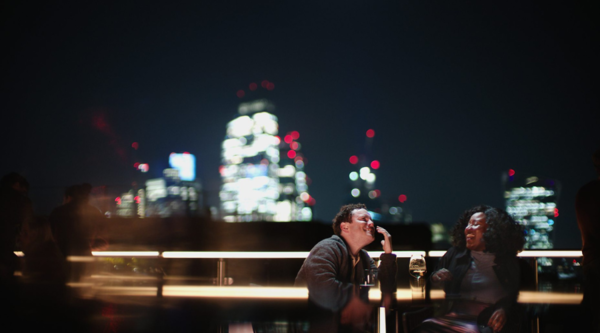 Two people sit against a cityscape at night, laughing