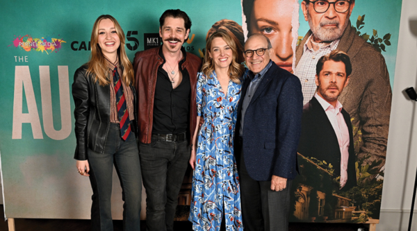 A white woman with blonde hair, a man with dark hair and a moustache, a white woman in a blue patterned dress and an older white man in a suit stand linking arms against the artwork for The Au Pair