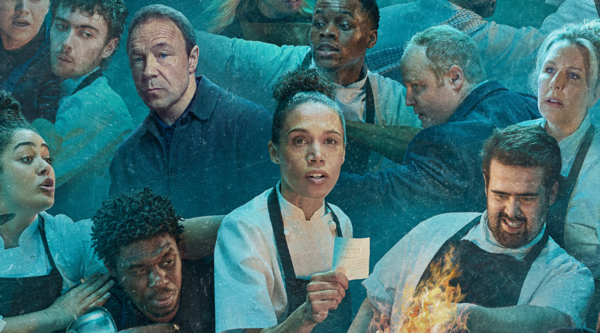 The cast of Boiling Point stand in an ensemble in a blue-ish light, all of them in kitchen attire and looking stressed