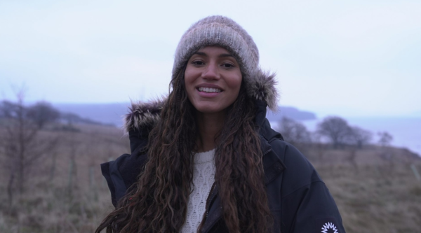 Hope, a British-Nigerian woman in her thirties, stands outdoor smiling in a coat and grey wooly hat