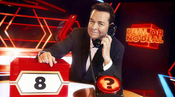Stephen Mulhern poses with a phone to his ear next to a box labelled '8', in front of the logo for Deal or No Deal