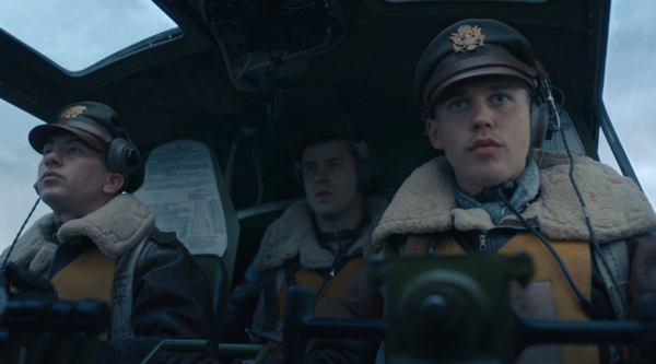 Barry Keoghan, a white man in his early 30s, sits in the cockpit of a WWII bomber with Austin Butler, a white man in his early 30s. Sat behind them is another young white man, all three of them in WWII airman outfits