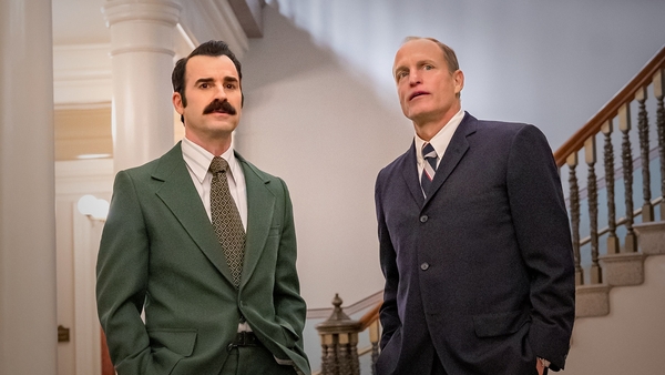 Woody Harrelson and Justin Theroux stand speaking near a grand staircase