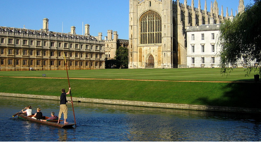 A man punts down a river in front of a church in Cambridge