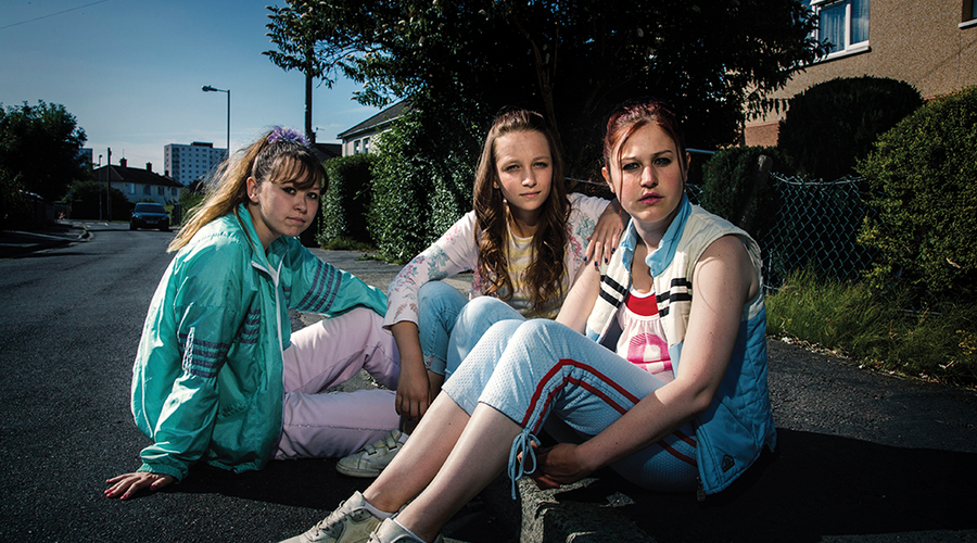 The cast of Three Girls sit on a curb