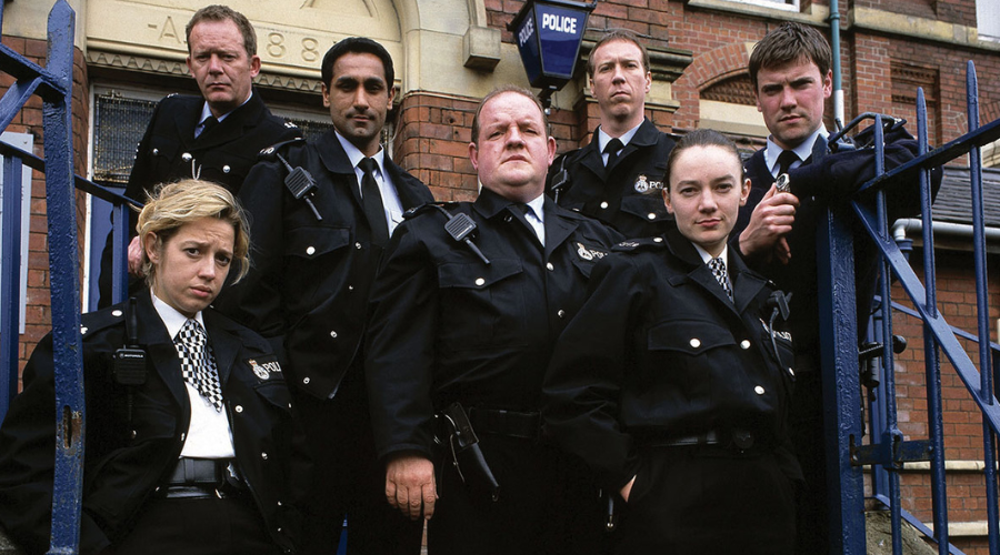 The cast of The Cops look into the camera, wearing police uniform and looking serious