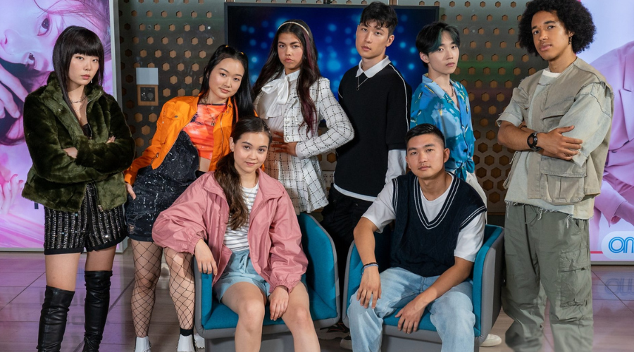 Eight teenagers sit and stand, looking into the camera