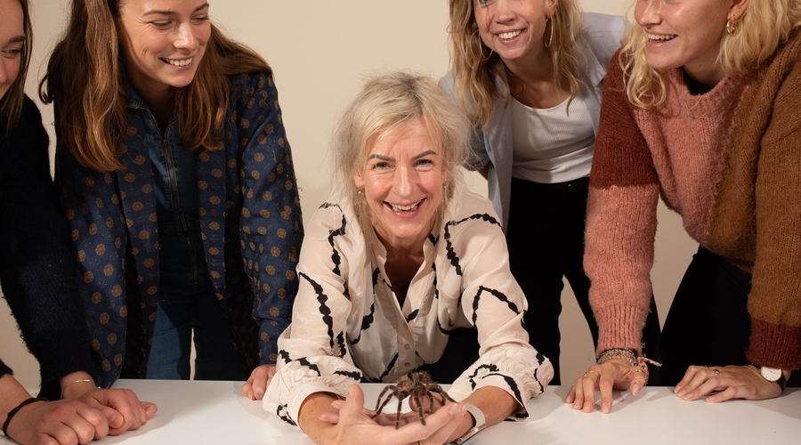 A woman sits holding a spider, laughing, surrounded by a few other people