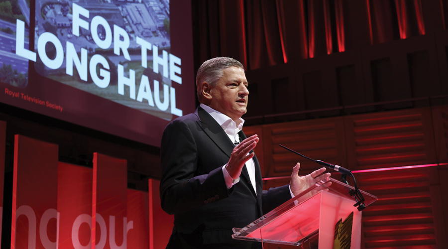 Ted Sarandos stands at a podium, delivering a talk at the RTS London Convention, beneath a screen on which text reading "FOR THE LONG HAUL" is visible