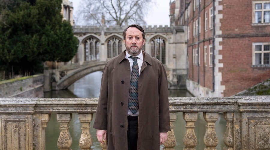 David Mitchell stands on a bridge in Cambridge, looked concerned in character as puzzler-turned-detective Ludwig