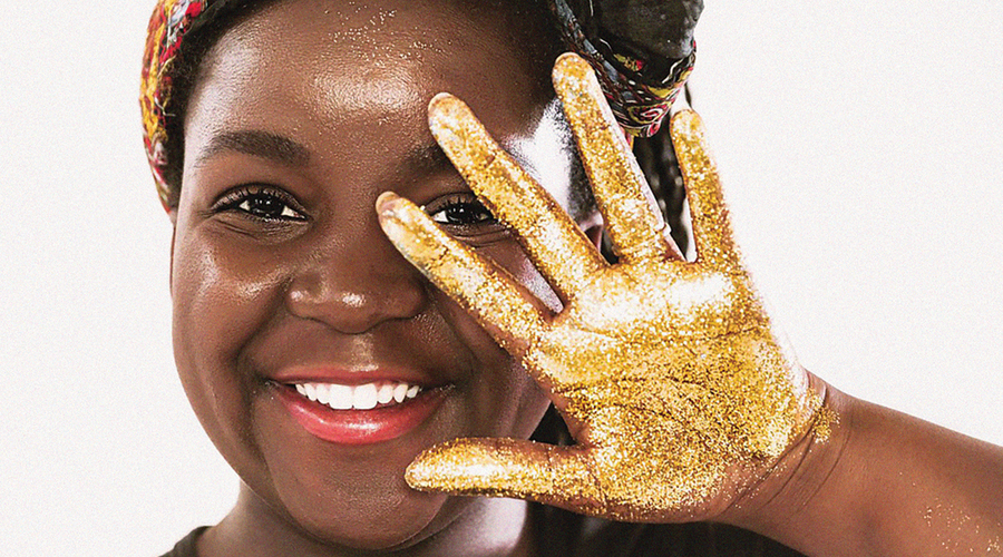 A smiling woman holds her hand out in a wave, covered in gold glitter