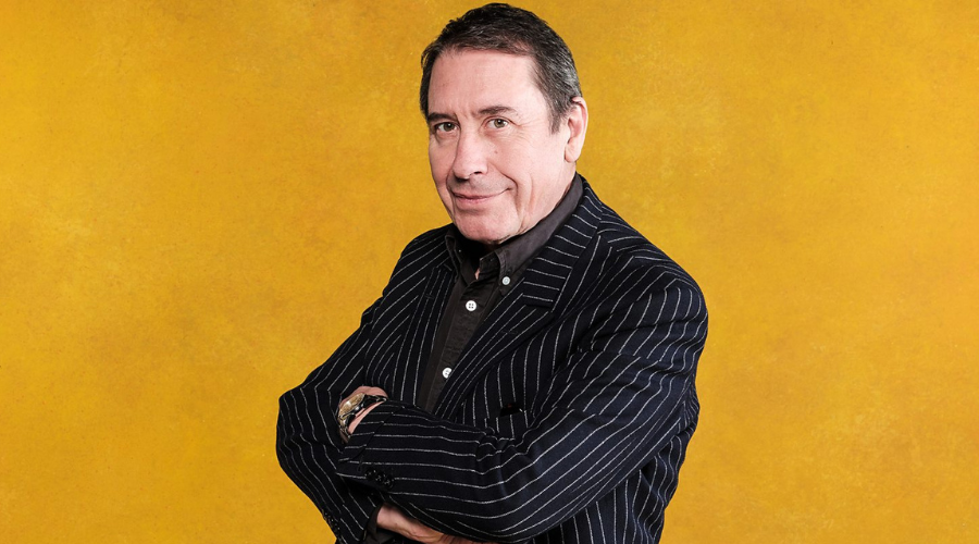 Jools Holland stands in front of a golden backdrop in a black pinstriped suit