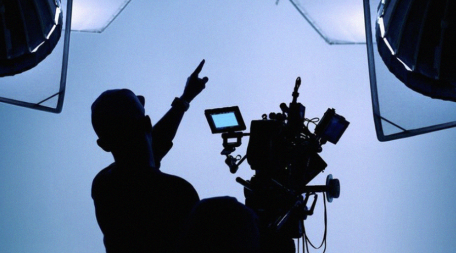 A man in silhouette points upwards, next to a camera, also in silhouette
