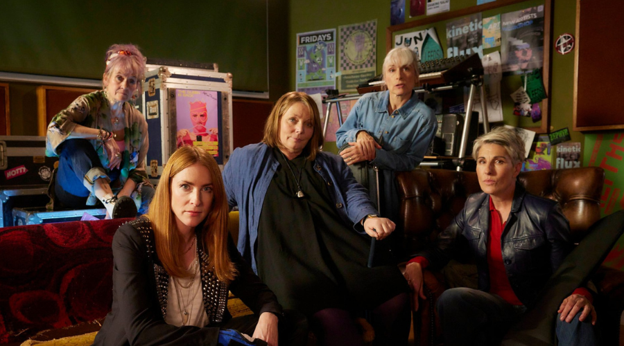 Lorraine Ashbourne, Rosalie Craig, Joanna Scanlan, Amelia Bullmore and Tamsin Greig, all white women between their forties and sixties, sit or lean on sofas and flight cases, looking into the camera