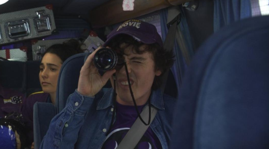 Sam Campbell squints as he looks through a lens, Lara Ricote looking desolate behind him, both of them sat in a packed van