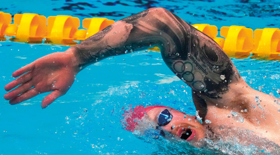 A swimmer doing some kind of front crawl looks to the side, half his face submerged in the water, his hand poised to re-enter the water