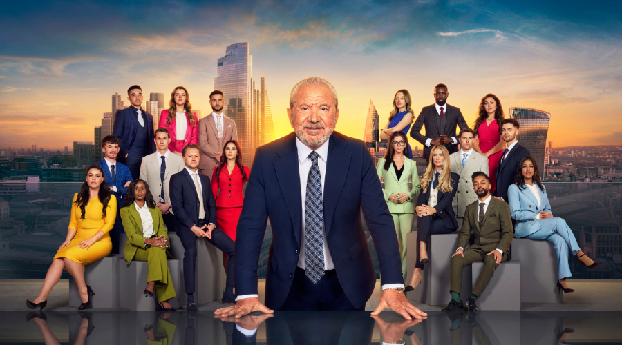 Alan Sugar, a white man in his seventies, stands in front of the contestants for the 19th series of The Apprentice, the scene set against a London skyline with the sun low in the sky, covered by Sugar's body 