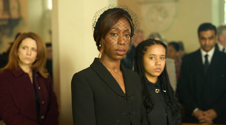 Nikki Amuka-Bird and Eden Hollingsworth stand in a church in funeral attire, unsmiling