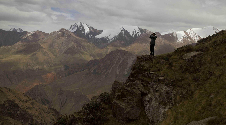 A man with binoculars stands on a mountain range