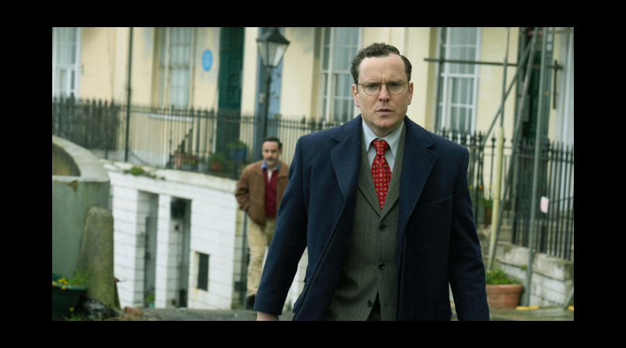 Joshua McGuire, a white man in his thirties, walks up a road in a suit, looking confused or distressed, while a man follows him