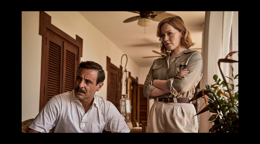 Emun Elliott, a white man in his forties, and Charlotte Spencer, a white woman in her thirties, frown at something off camera, the two wearing clothes that have light, earthy tones