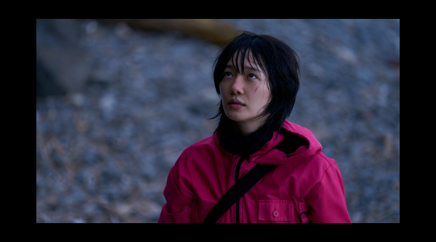 Park Gyu-young, a South Korean woman in her early thirties, looks up at something off-camera, wearing the pink jumpsuit worn by guards in the game