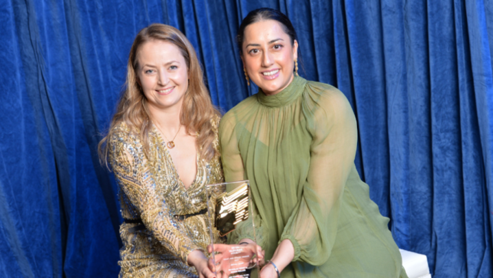 Two women pose with their RTS Craft & Design award: on the left, a woman with long blonde curly hair wearing a sparkly dress smiles, and on the right, a woman with dark brown hair in a green dress smiles