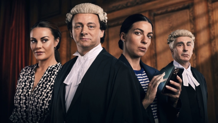 Two men dressed as lawyers in robes and a barrister's wig, stand with two women one of which is holding a phone