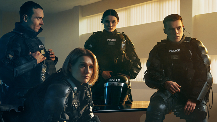 Martin McCann (Stevie), Siân Brooke (Grace), Katherine Devlin (Annie) and Nathan Braniff (Tommy) sit and stand around a desk in police uniform in a police office
