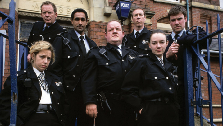 The cast of The Cops look into the camera, wearing police uniform and looking serious