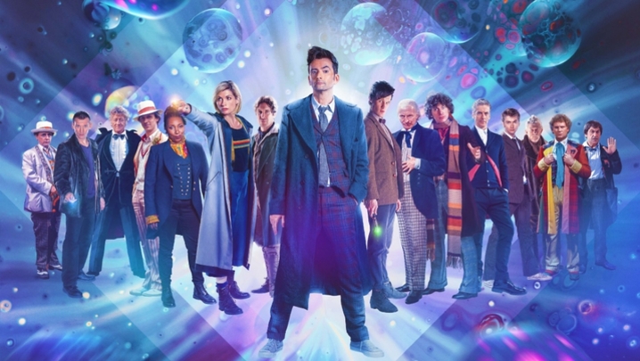 The Sixteen Doctors from BBC sci-fi hit Doctor Who, including the War Doctor and the Fugitive Doctor, stand in a line in front of a blue and pink backdrop