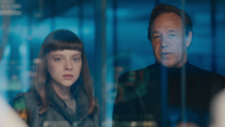 A woman, Shira Haas as Iris Maplewood, and a man, Stephen Graham as Elias Mannix, stand side by side in a blue room, in a still from Netflix series Bodies