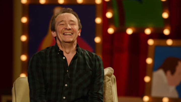 Paul Whitehouse laughs in front of a set with individual orange lightbulbs