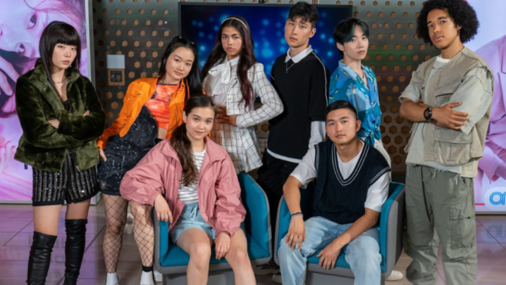 Eight teenagers sit and stand, looking into the camera