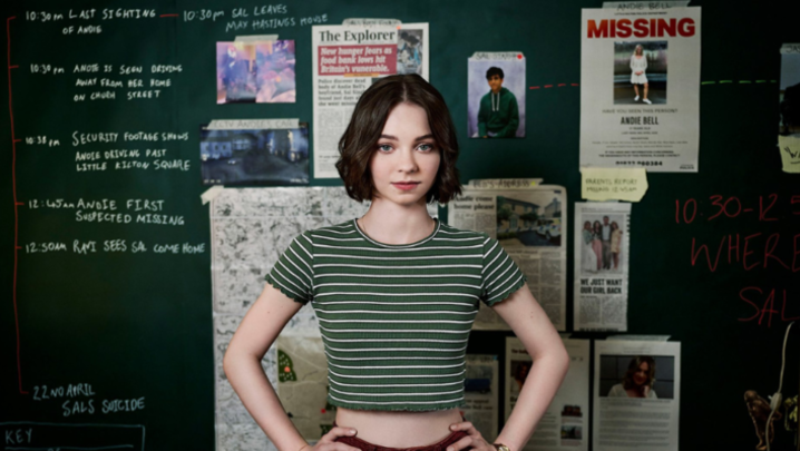 Pip Fitz-Amobi stands in front of a green chalkboard with a timeline of events and newspaper clippings 