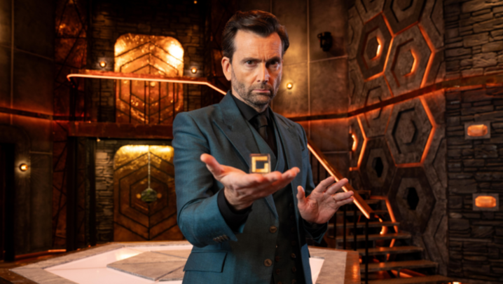 David Tennant stands in a room holding a cube