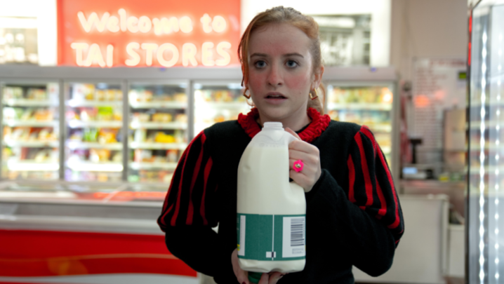 Jen from Extraordinary stands in a shop, red in the face, holding a bottle of milk