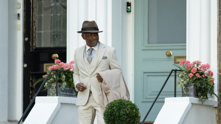 Lennie James walks down the steps of a house in a white and grey checkered suit