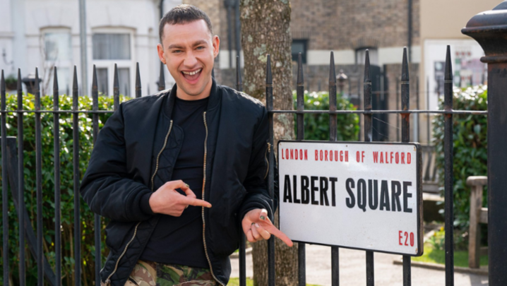 Olly Alexander points excitedly at the street sign for Albert Square
