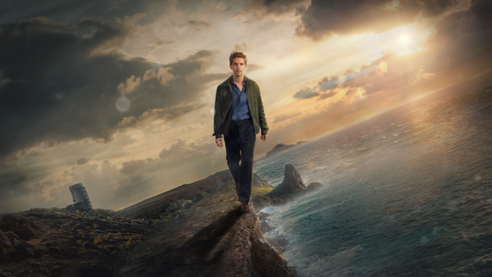 In a stylised image, Damien Molony, a white man in his forties, walks towards the camera down an island coast, the landscape titled at 30 degrees, while Molony stands level, and much bigger than the coast 