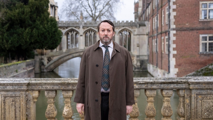 David Mitchell stands on a bridge in Cambridge, looked concerned in character as puzzler-turned-detective Ludwig