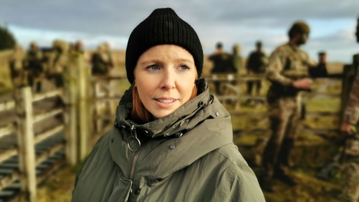 Stacey Dooley stands in the foreground, with soldiers training behind her