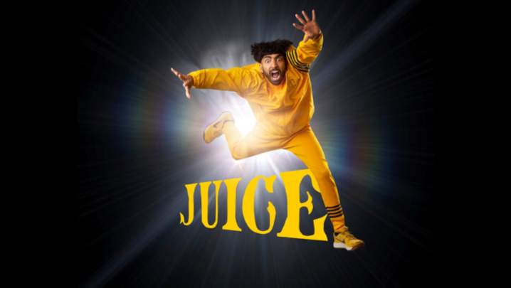 Mawaan Rizwan stands in front of a black backdrop, arms spread wide and mouth open in shock. 'Juice' is written in yellow text next to him