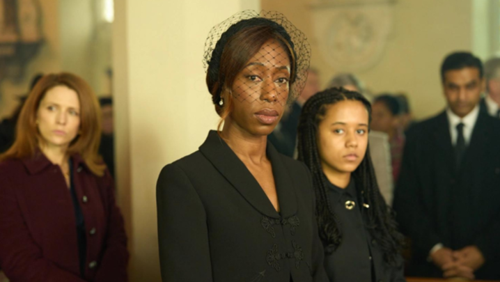 Nikki Amuka-Bird and Eden Hollingsworth stand in a church in funeral attire, unsmiling