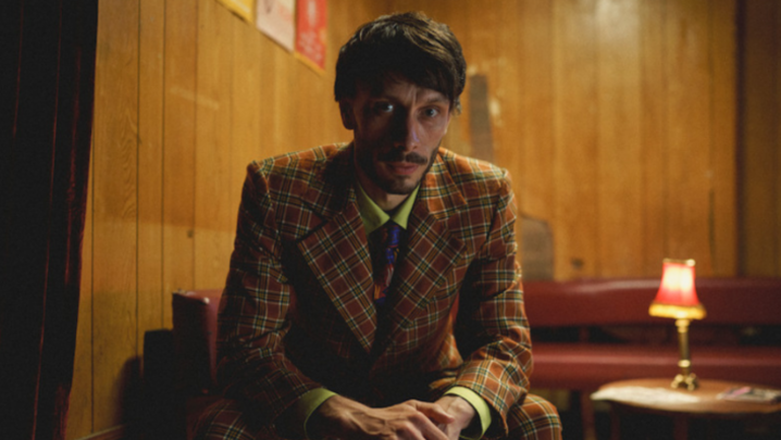 Richard Gadd, a white man in his thirties, sits indoors looking into the middle distance, wearing a garish suit