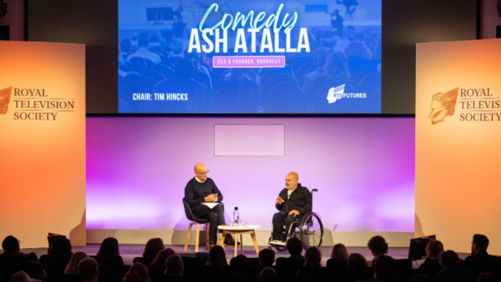 Tim Hincks and Ash Atalla sit on a stage in front of a silhouetted crowd, beneath a big screen with 'Comedy, Ash Atalla, CEO and Founder of Roughcut' written on it