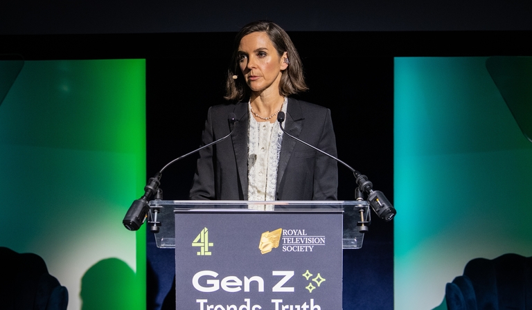 A woman in her 50s with dark hair and wearing a black blazer and white shirt stands at a lecturn covered with the words: 'Gen Z: Trends, Truth and Trust'