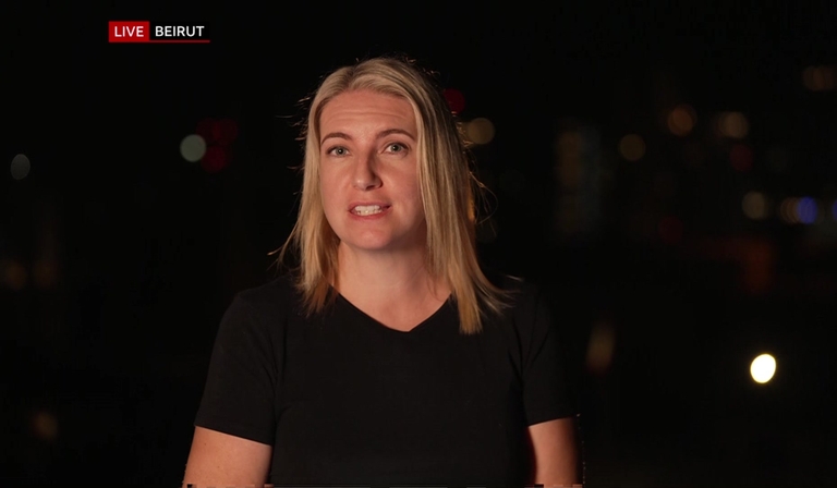 Anna Foster stands in front of a black backdrop outdoors, the words "LIVE BEIRUT" superimposed in the top left hand corner